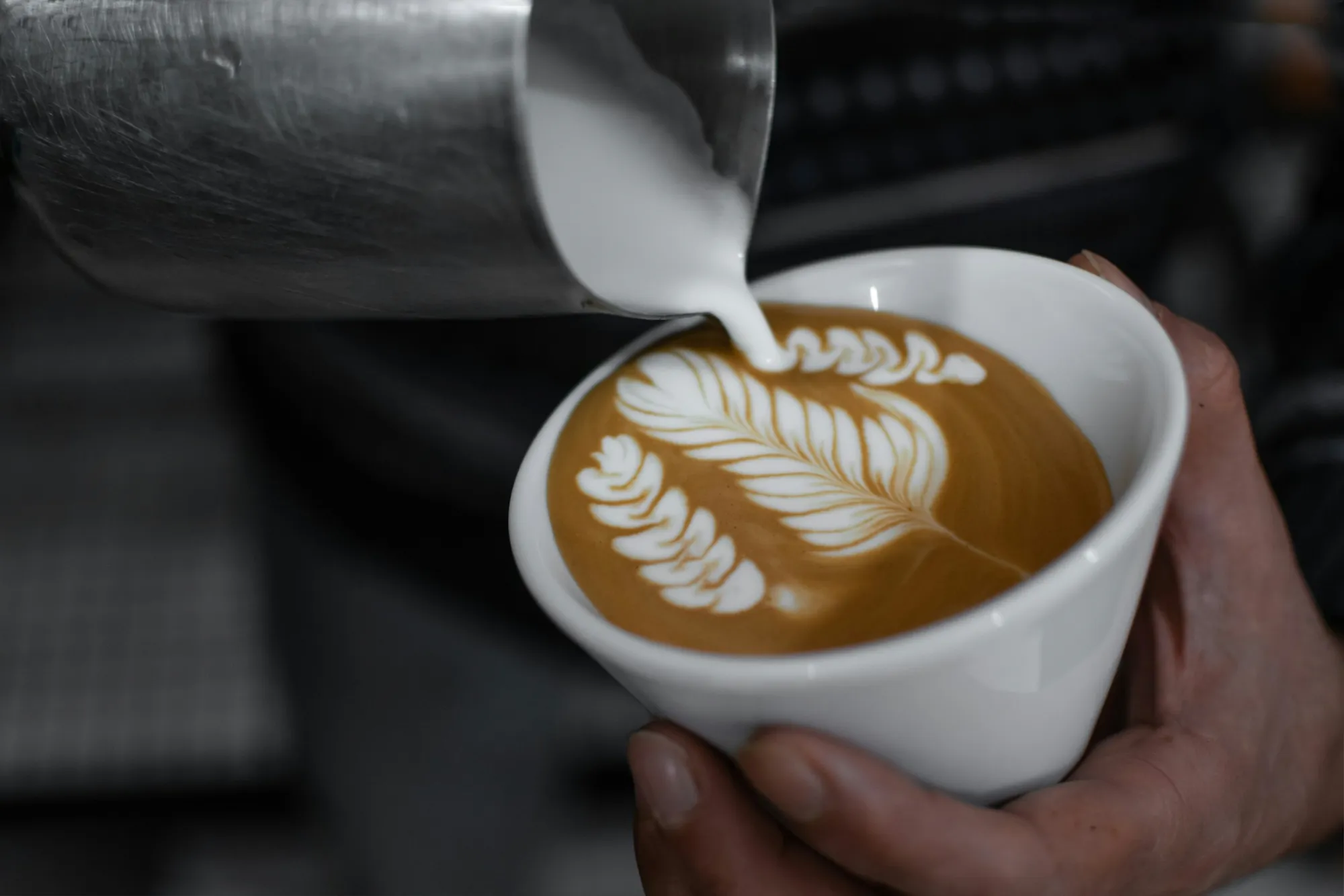 Barista sirviendo latte art en una taza blanca